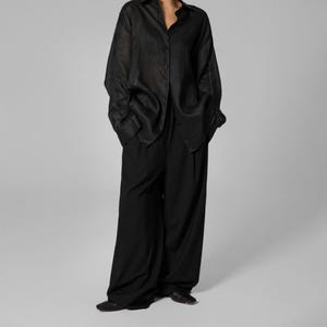 Pu&ograve; includere: Una camicia nera a maniche lunghe, ampia e con bottoni, con un paio di pantaloni neri a gamba larga.