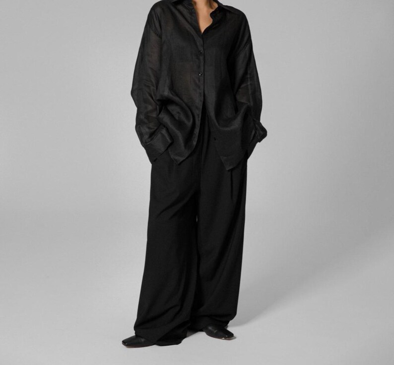 Pu&ograve; includere: Una camicia nera a maniche lunghe, ampia e con bottoni, con un paio di pantaloni neri a gamba larga.