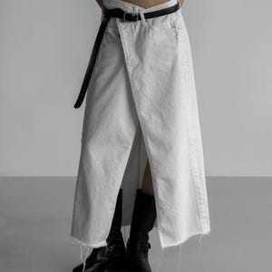 May include: White denim wrap skirt with a raw hem, paired with a black belt and black boots. The skirt has a unique asymmetrical design. The outfit is simple and stylish, suitable for various occasions.