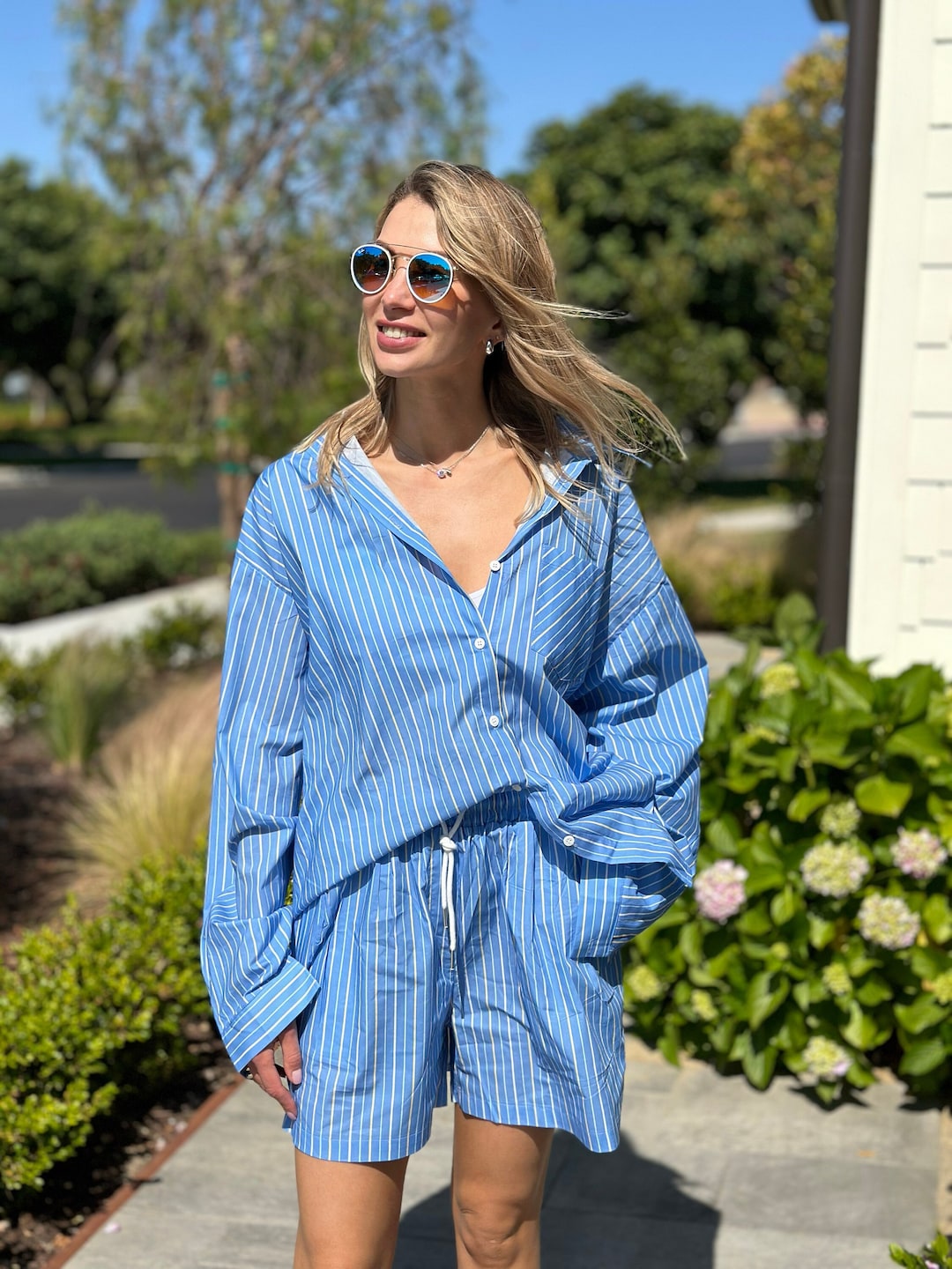 Chic young woman in a blue striped shirt and shorts enjoys summer, showcasing trendy summer outfits for women.