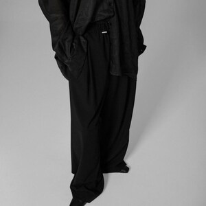 Pu&ograve; includere: Una camicia nera a maniche lunghe con chiusura a bottoni e un paio di pantaloni neri a gamba larga.