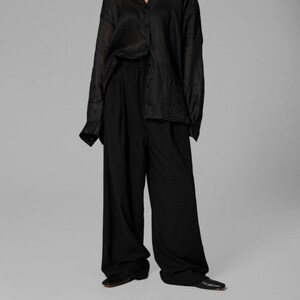 Pu&ograve; includere: Una camicia nera oversize con bottoni e maniche lunghe. La camicia &egrave; abbinata a pantaloni neri a gamba larga.