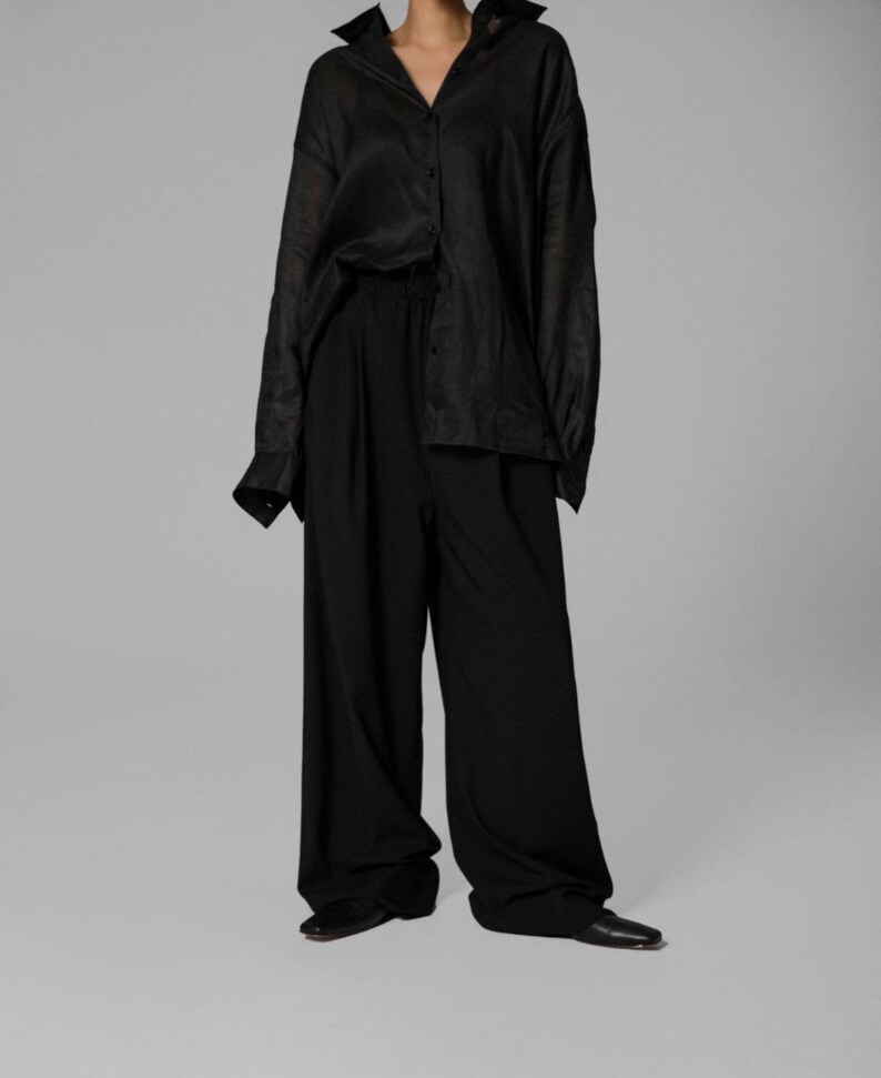 Pu&ograve; includere: Una camicia nera oversize con bottoni e maniche lunghe. La camicia &egrave; abbinata a pantaloni neri a gamba larga.