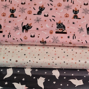 May include: Three stacked bolts of fabric. The top bolt is light pink with black cats wearing orange hats, pumpkins, spiderwebs, and bats. The middle bolt is white with small pink and black stars. The bottom bolt is black with white ghosts and stars.