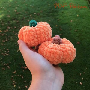 May include: Two crocheted pumpkins in a peach color. One pumpkin has a green stem and the other has a brown stem.