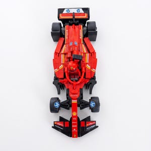 May include: A red Formula 1 race car model featuring black tires, a driver figure in the cockpit, and various sponsor logos including HP, Santander, and V-Power. The vehicle displays a detailed aerodynamic design with a front wing and rear spoiler.
