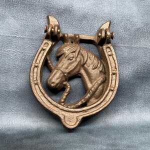 May include: A cast iron door knocker shaped like a horseshoe with a horse's head in the center. The knocker is painted in a bronze color.