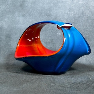 Pode incluir: Uma tigela de cerâmica azul e laranja com um detalhe prateado. A tigela tem a forma de uma onda e tem um buraco no centro.