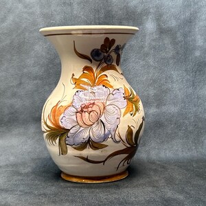 May include: A white ceramic vase with a floral design. The vase has a wide mouth and a rounded body. The flowers are painted in shades of blue, pink, orange, and green.