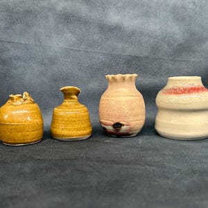 Pode incluir: Quatro pequenos vasos de cerâmica em diferentes cores e estilos. Os vasos são todos feitos à mão e têm um aspeto rústico único.