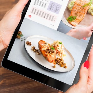 May include: A tablet displaying a recipe for salmon with celery puree. The recipe includes ingredients and instructions. The image also shows a plate of salmon with celery puree and a plate of sweet potato with lentils and cabbage.