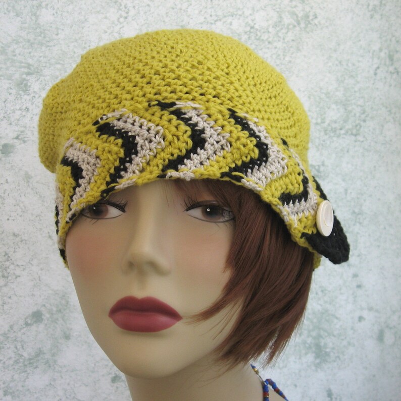 May include: A yellow crocheted hat with a black and white chevron pattern. The hat has a brim and a button on the side.