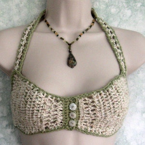 May include: A crocheted halter top with a green and white color scheme. The top has a button closure in the front and a delicate crocheted design.