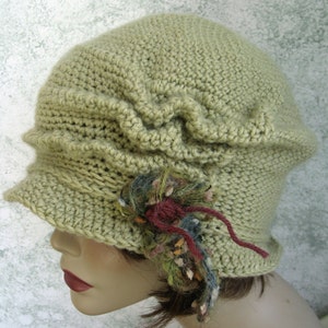 Puede incluir: Un sombrero cloche de crochet verde con un adorno floral decorativo.
