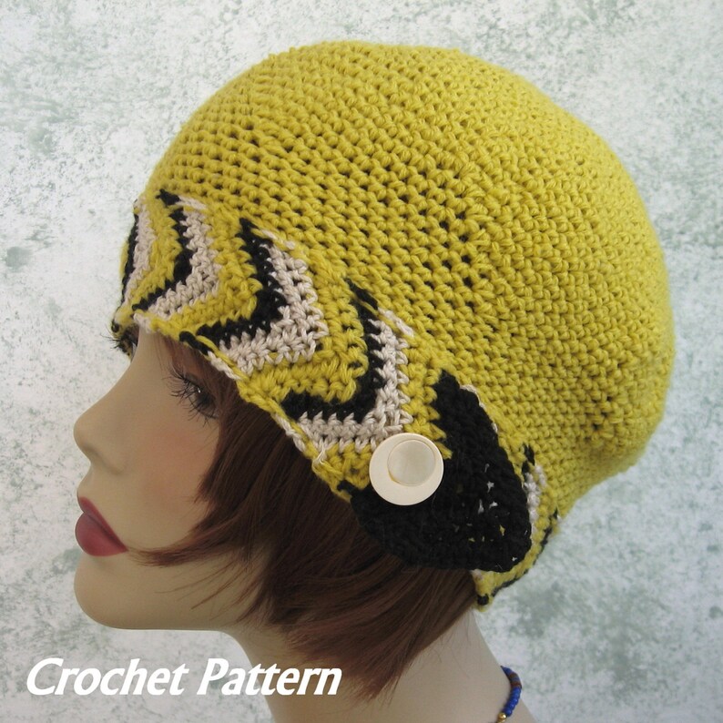 May include: A yellow crochet beanie with a black and white geometric pattern around the brim. The beanie has a white button on the side.