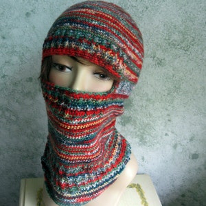 May include: A red, green, and white striped knitted balaclava with a hole for the eyes. The balaclava is worn on a mannequin's head.
