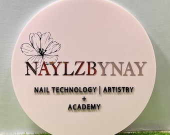 Może przedstawiać: Okrągły, jasnoróżowy znak z napisem "NAYLZBYNAY" w miedzianych literach. Poniżej słowa "NAIL TECHNOLOGY | ARTISTRY + ACADEMY" są w kolorze czarnym. Czarny kwiatowy wzór zdobi lewy górny róg.