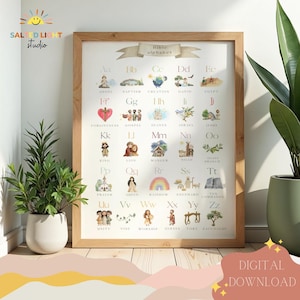 Pode incluir: Uma impressão emoldurada com o alfabeto bíblico com ilustrações em aquarela. Cada letra tem uma palavra e imagem correspondente, como "Anjo" para A e "Batismo" para B. A impressão está em uma moldura de madeira clara e inclui o texto "DOWNLOAD DIGITAL".