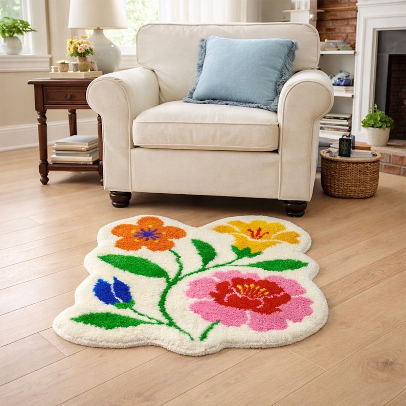 May include: A floral-shaped rug with a cream background and colorful flowers. The flowers are orange, yellow, pink, and blue, with green stems and leaves. The rug is placed on a light wood floor in a living room setting.