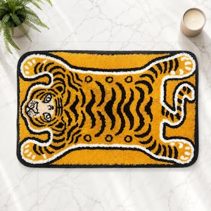 Puede incluir: Una alfombra de baño rectangular con un diseño de tigre con mechones en colores amarillo vibrante, negro y blanco. El tigre se muestra en una vista plana desde arriba con las extremidades extendidas, rayas negras y un borde blanco.