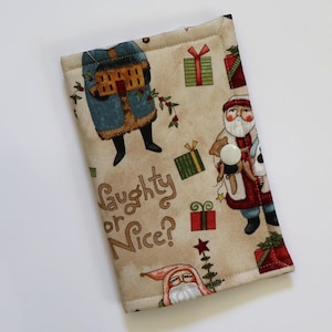 May include: A rectangular fabric cover featuring a beige background with a Christmas-themed print of Santa Claus figures, wrapped gifts, and the text Naughty or Nice? The cover is secured with a single white snap button closure on the front.