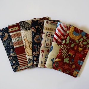 May include: A collection of six rectangular fabric pouches arranged in a fan shape. The pouches feature various patterns including floral prints, a cat illustration, American flag motifs, and text reading "In God is our trust" and "GLORY".
