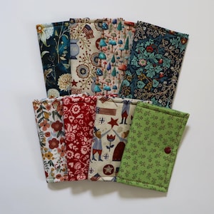May include: A collection of eight rectangular fabric pouches featuring various patterns including floral prints, mushroom motifs, patriotic themes with stars and stripes, and intricate botanical designs. Each pouch is stitched and has a button closure.