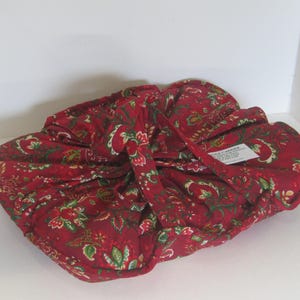 Puede incluir: Una bolsa de tela roja con un estampado floral en verde y blanco. La bolsa está atada con una correa de tela a juego. La bolsa está hecha de un material suave y acolchado.