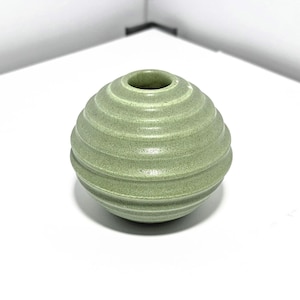 Könnte beinhalten: Eine kleine, runde, grüne Keramikvase mit einer strukturierten, gerippten Oberfläche.