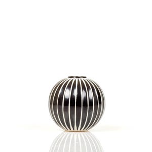 Könnte beinhalten: Eine kugelförmige Vase mit schwarz-weißen Streifen. Die Vase hat eine glänzende Oberfläche und eine schmale Öffnung oben. Die weißen Streifen sind vertikal und gleichmäßig angeordnet, wodurch ein ansprechendes Muster entsteht. Die Vase steht auf einer weißen Oberfläche.