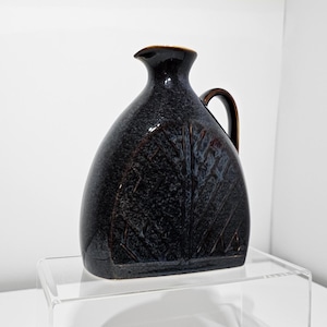 May include: A dark blue ceramic pitcher with a leaf design. The pitcher has a brown rim and handle.