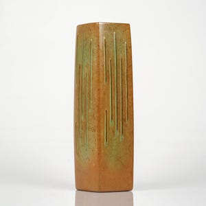 Puede incluir: Un jarrón rectangular de cerámica en tonos marrón y verde. Ranuras verticales recorren los lados. El jarrón tiene una forma ligeramente cónica y un acabado mate. Un objeto decorativo para el hogar.