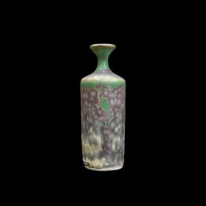 May include: A tall ceramic bottle with a narrow neck and a flared rim. The surface features a mottled glaze with blended shades of deep forest green, muted purple, and earthy beige, creating a textured, cloud-like pattern across the cylindrical body.