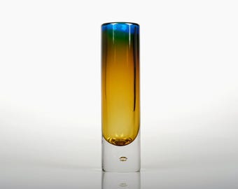 May include: A tall, cylindrical glass vase with a gradient of colours. The top is blue, transitioning to green, then yellow, and the base is clear. The vase has a small, rounded base with a bubble detail.