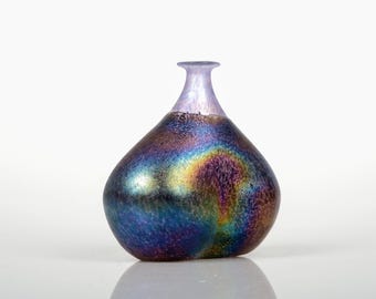 May include: A decorative glass vase with an iridescent finish. The vase has a rounded body and a slender neck. The colors shift from deep blues and purples to rainbow hues. The vase is approximately 15 cm tall.