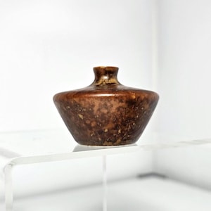 May include: A small, brown ceramic vase with a mottled glaze. The vase has a wide, rounded base and a narrow neck.