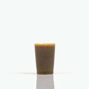 Peut inclure: Une petite tasse cylindrique en céramique dotée d'un vernis réactif qui passe d'un vert olive profond et terreux à la base à une teinte miel chaud et plus claire près du bord lisse et arrondi, créant un subtil effet de dégradé.