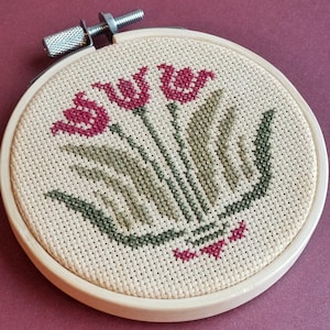 May include: A cross-stitch embroidery hoop with a design of three red tulips with green leaves and stems.