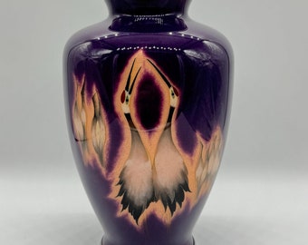 Peut inclure: Un vase décoratif violet avec une finition brillante. Le vase présente un motif de grues en vol, avec des détails pêche et noirs. Les bords supérieur et inférieur sont argentés. Une belle pièce pour la décoration intérieure.