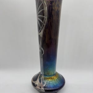 Pu&ograve; includere: Un vaso alto in vetro artistico iridescente con base bulbosa e collo sottile. Il vaso presenta un design Art Nouveau argentato e una sfumatura di colore dal viola al blu all'oro. Il vaso &egrave; alto circa 30 cm.