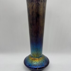 Pu&ograve; includere: Un vaso alto di vetro iridescente con la parte superiore svasata e una base arrotondata. Il vaso passa da un viola intenso nella parte superiore a un blu e oro vibranti nella base. Il vaso &egrave; alto circa 30 cm.