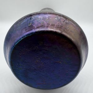 Pu&ograve; includere: Un vaso rotondo e iridescente con una superficie strutturata. Il vaso passa da un viola intenso alla base a una tonalit&agrave; pi&ugrave; chiara e scintillante verso l'alto. Il vaso ha un corpo ampio e arrotondato e un collo stretto.
