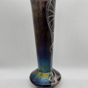 Pu&ograve; includere: Un vaso alto in vetro artistico iridescente con la parte superiore svasata e una base bulbosa. Il vaso presenta una combinazione di colori marrone scuro e viola con abbellimenti argentati in stile Art Nouveau. Il vaso &egrave; alto circa 30 cm.
