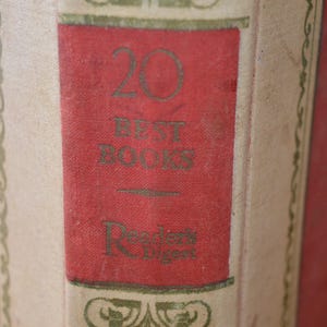 Op de afbeelding: Close-up van een boekenrug met een rode achtergrond en een crèmekleurig middenpaneel. Het paneel bevat de tekst "20 BEST BOOKS" en "Reader's Digest" in groene letters, met decoratieve randen.