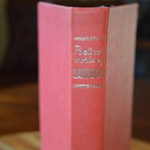 Op de afbeelding: Een vintage boek met een rode kaft en rug. De rug bevat de titel "Poetical works of LAWSON" in gouden letters. De pagina's van het boek zijn lichtbruin van kleur. Het boek is waarschijnlijk een verzameling gedichten.