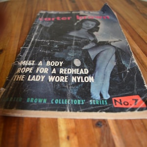 May include: Vintage Carter Brown Collectors' Series No. 7 book cover. The cover features a black and white image of a woman and text that reads "Meet a Body, Rope for a Redhead, The Lady Wore Nylon."