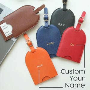 May include: A collection of personalized luggage tags in various colors, including brown, orange, blue, red, and black. Each tag features a buckle strap and a slot for an identification card. The tags are embossed with names or initials, with the text "Custom Your Name".