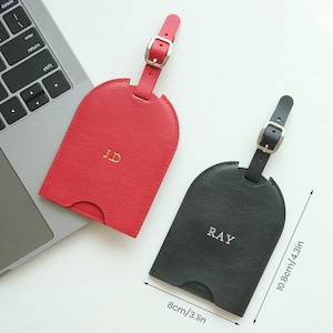May include: Two leather luggage tags, one red and one black, with silver buckles and straps. The red tag has the initials "JD" and the black tag has "RAY". Each tag is 3.1 inches wide and 4.3 inches long.