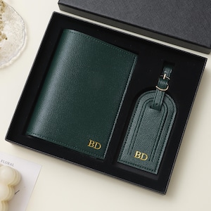 May include: A dark green passport holder and a matching luggage tag set presented in a black gift box. Both items feature a textured finish and the gold-embossed initials BD. The luggage tag includes a small gold-toned metal buckle strap.