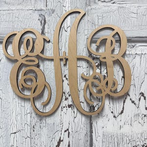 May include: A light brown wooden monogram cutout featuring the intertwined letters E, A, and B in a cursive script font. The letters are connected by flowing, decorative loops and swirls, creating a single, cohesive piece of laser-cut wood.